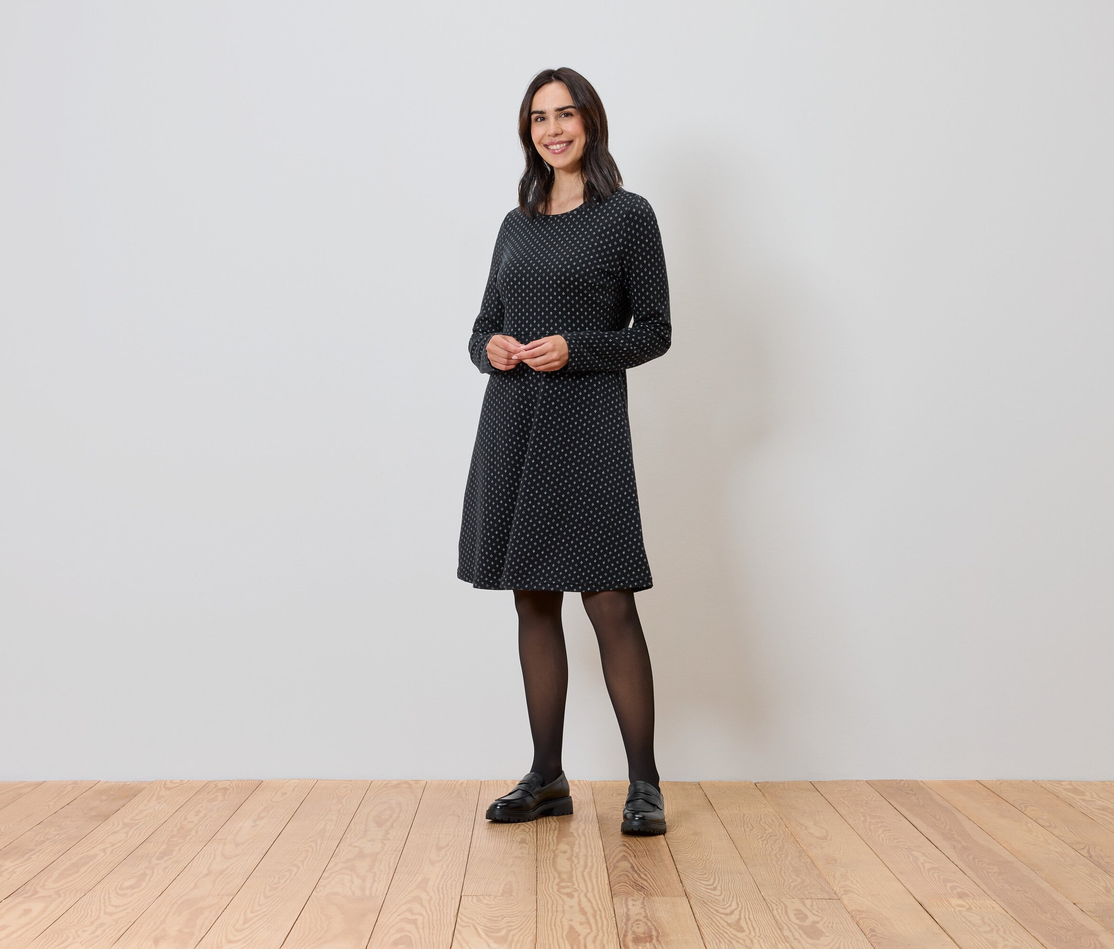 Žena stojí a má na sobě žakárové šaty se třpytivým efektem.