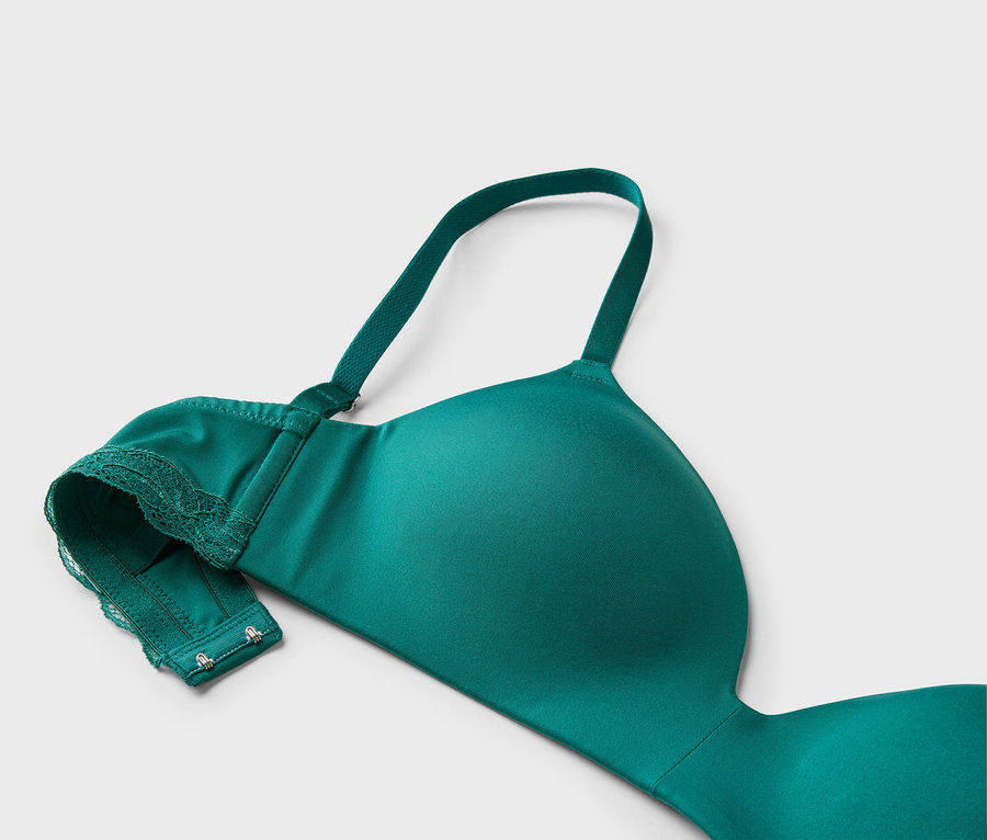 Detailní záběr na zelenou podprsenku s krajkou a nastavitelnými ramínky na světle šedém pozadí.