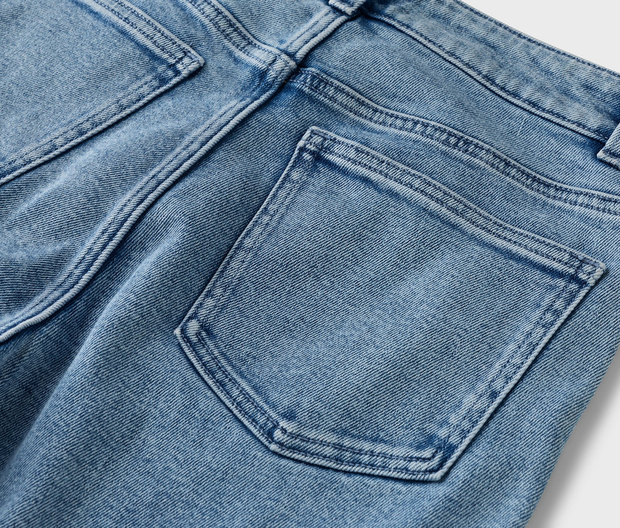 Detailní pohled na zadní část světle modrých džínů se zadními kapsami.