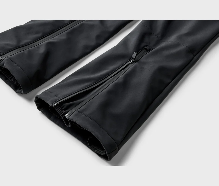 Detail dvou černých technických nohavic s bočními zipy po celé délce a elastickými manžetami. Jedna nohavice má navíc malou horizontální kapsu na zip.