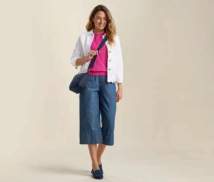Žena v džínových culottes, růžovém svetru a džínové bundě s anglickou krajkou. Modrá taška přes rameno a ladící nazouváky.