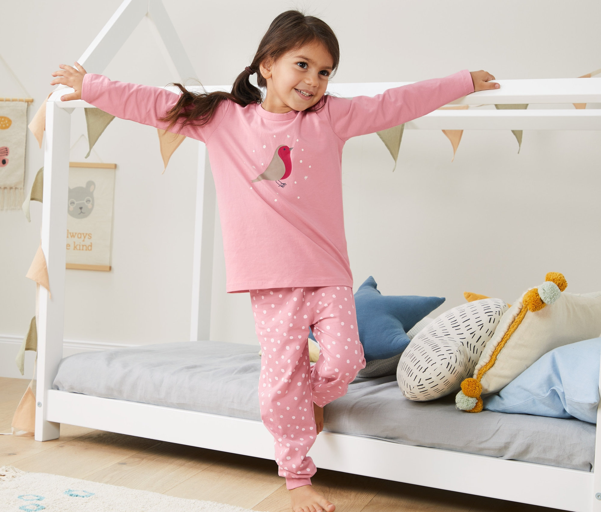 Dívka stojí v posteli a má na sobě růžové pyžamo Glow in the dark s biobavlnou.