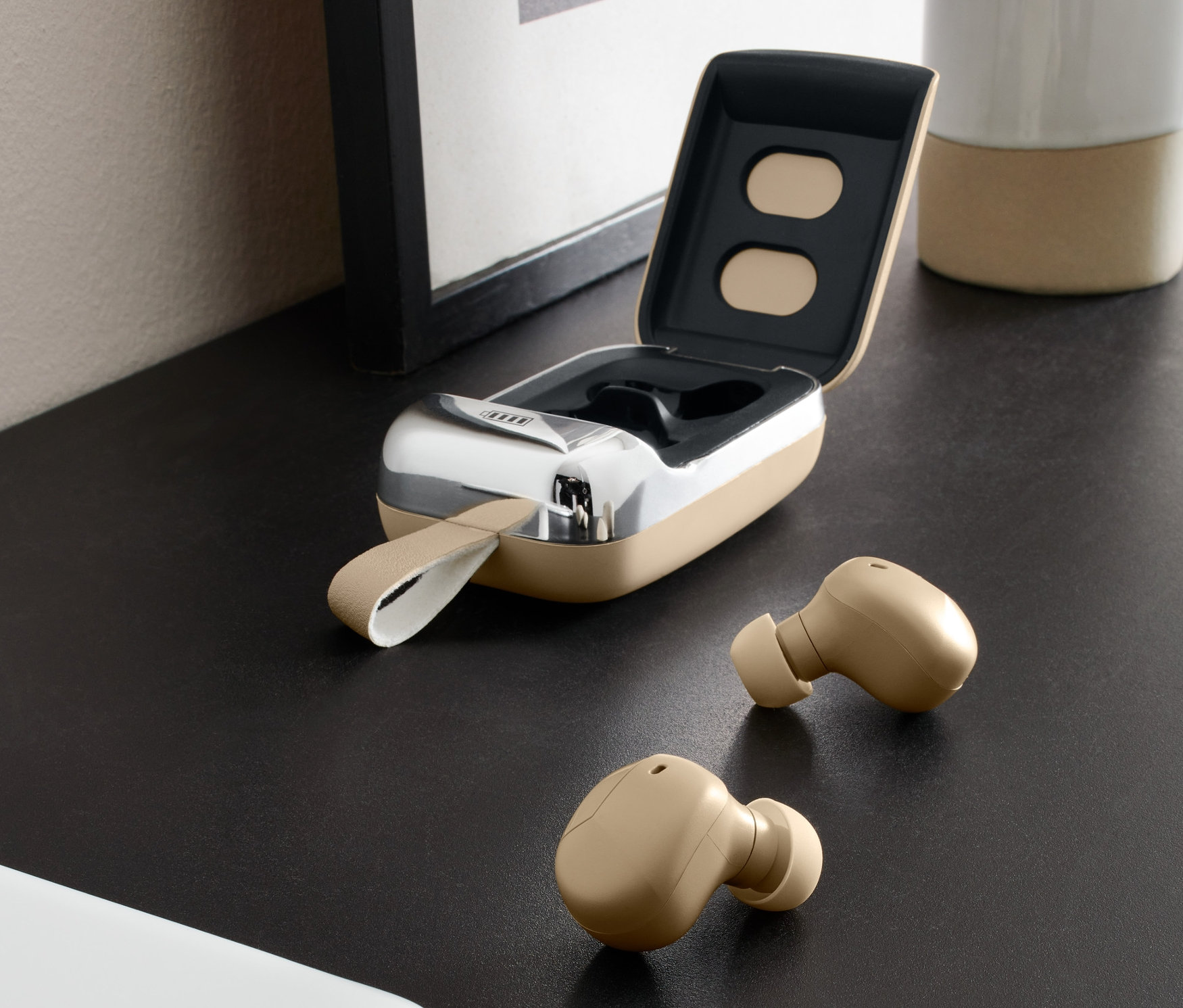 Dvoje béžová sluchátka TWS a otevřené pouzdro na stole vedle mobilního telefonu.