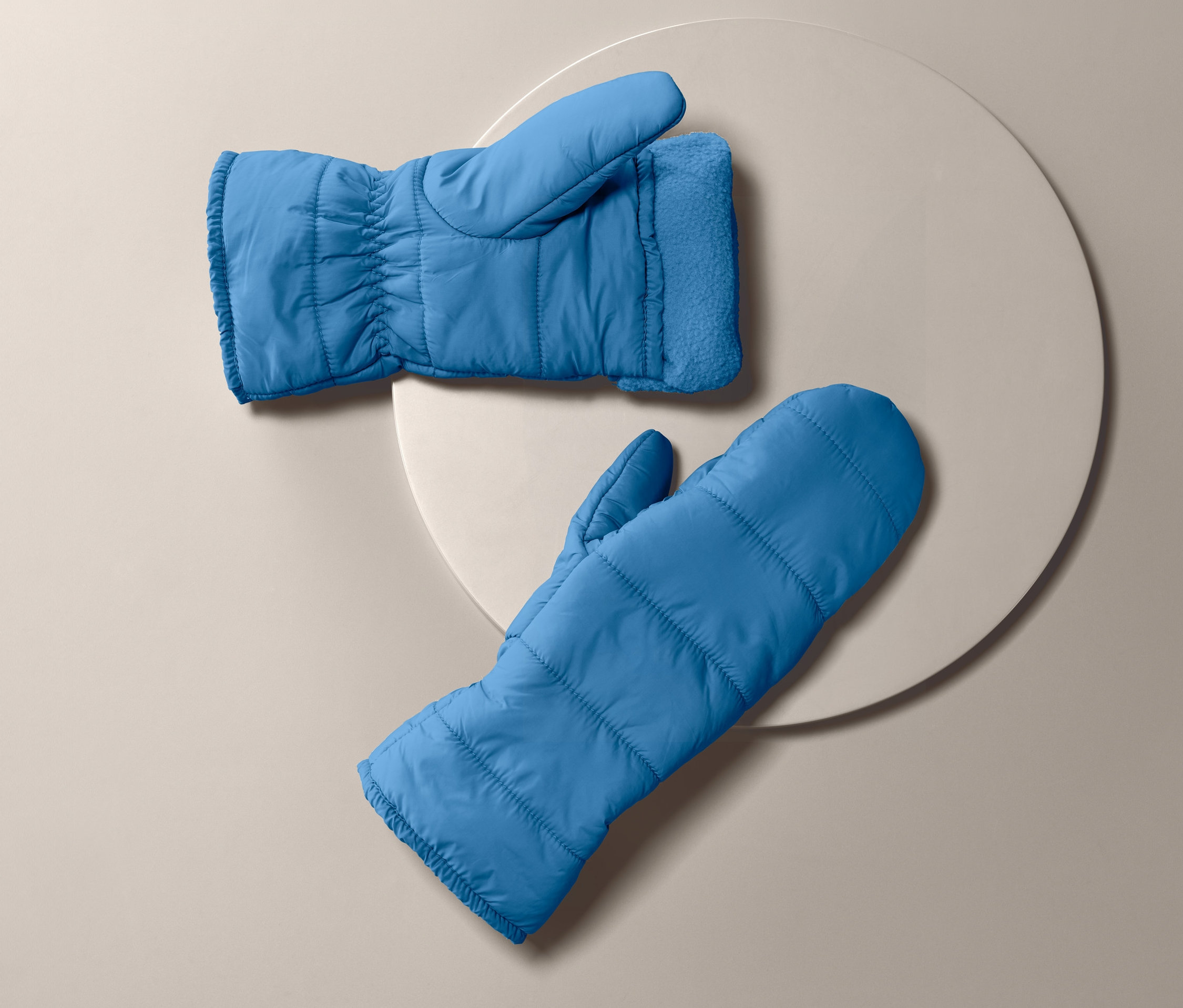 Dvě modré prošívané palčáky leží na béžovém pozadí.