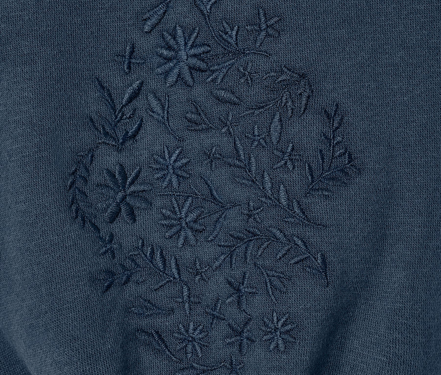 Detail těhotenské mikiny s květinovou výšivkou.