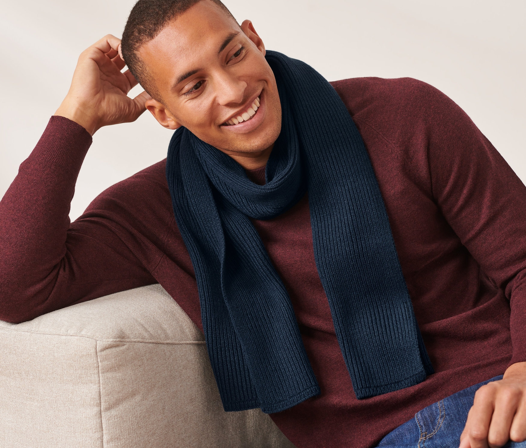 Muž sedí na gauči a má na sobě pletenou šálu námořnické modré barvy.