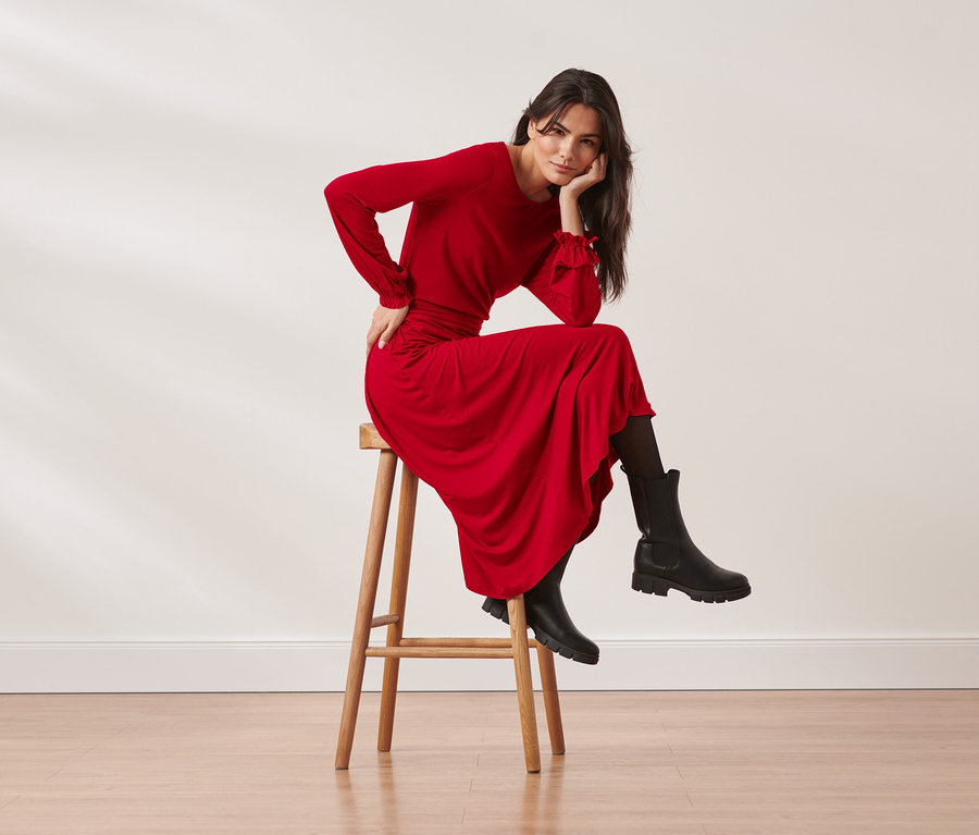 Žena sedí na stoličce v červených žerzejových midi šatech.