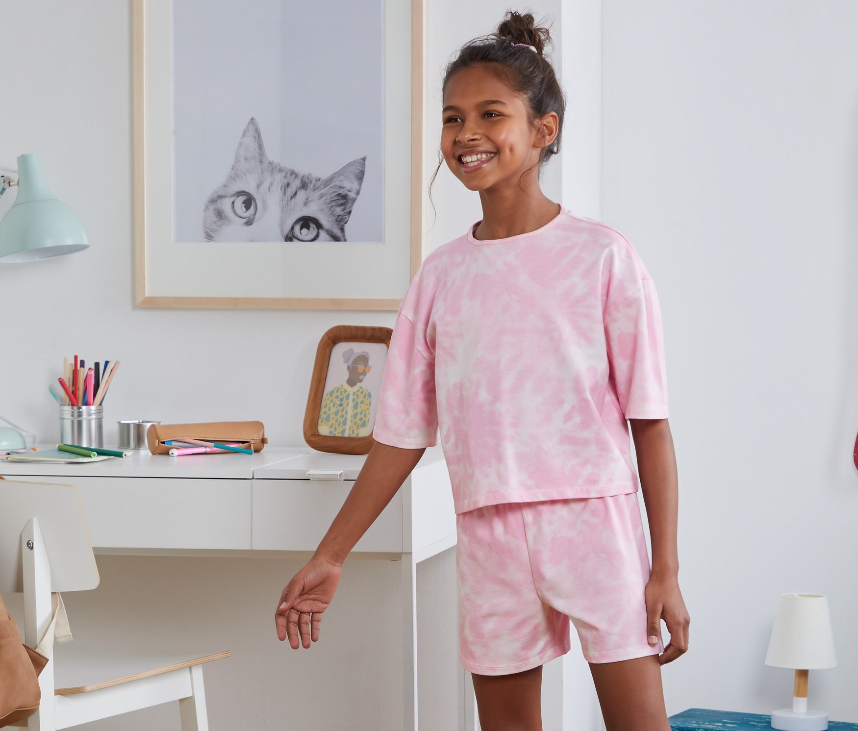 Usmívající se dospívající dívka pózuje v růžovém pyžamu z biobavlny v ložnici.