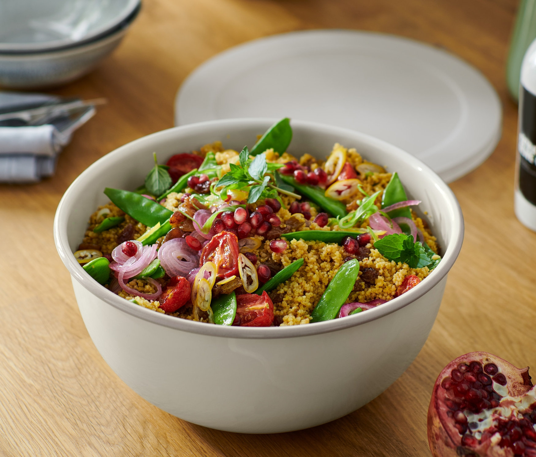 Salát v smaltované míse na servírování a přípravu, s víkem, na dřevěném stole s granátovým jablkem.