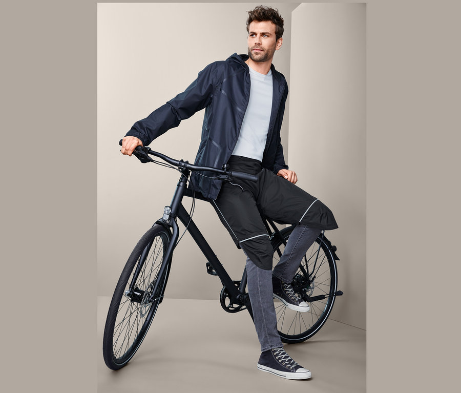 Muž sedí na kole a má na sobě unisexové návleky do deště.