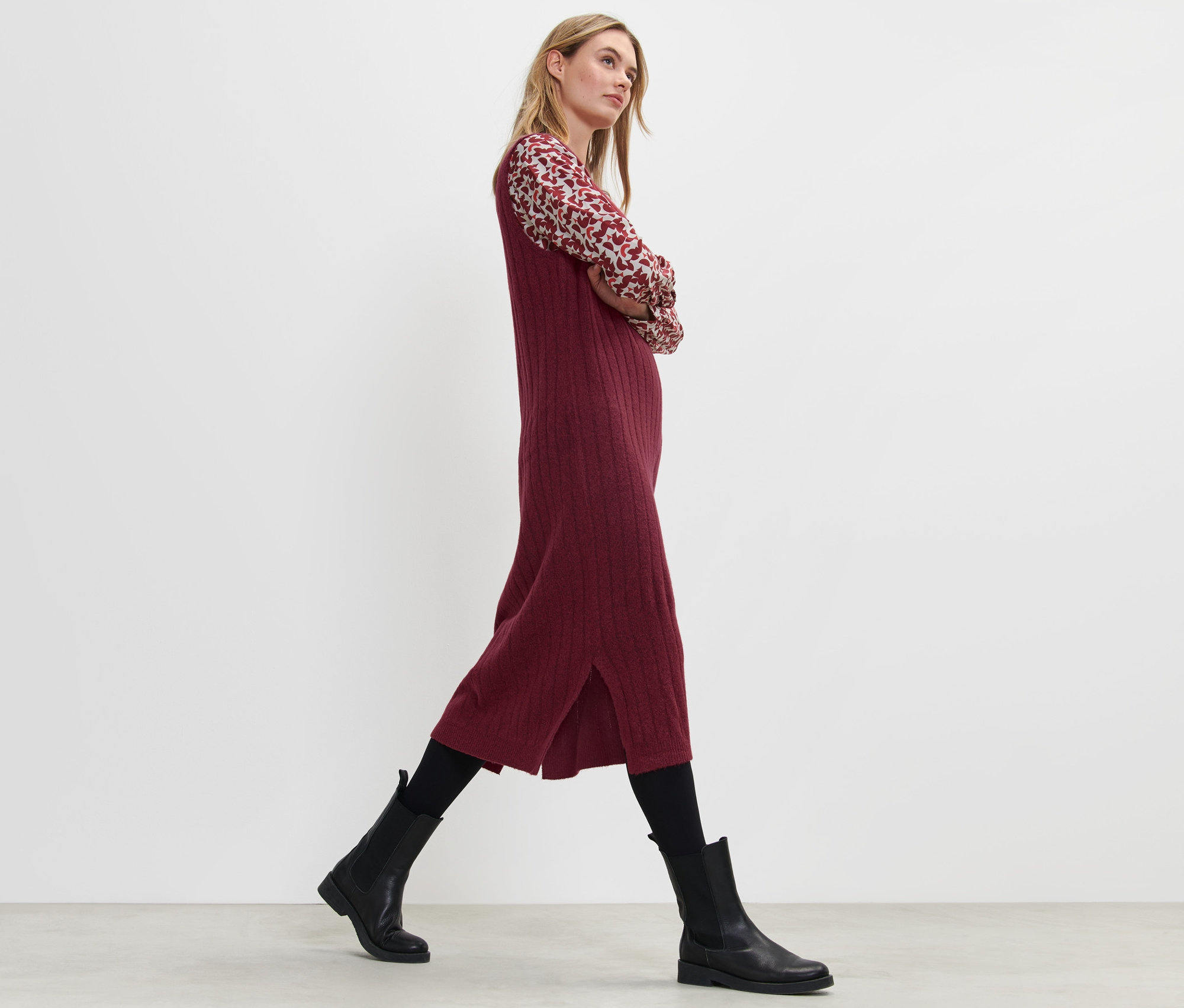 Blondýna kráčí a má na sobě červené žebrované pletené šaty.