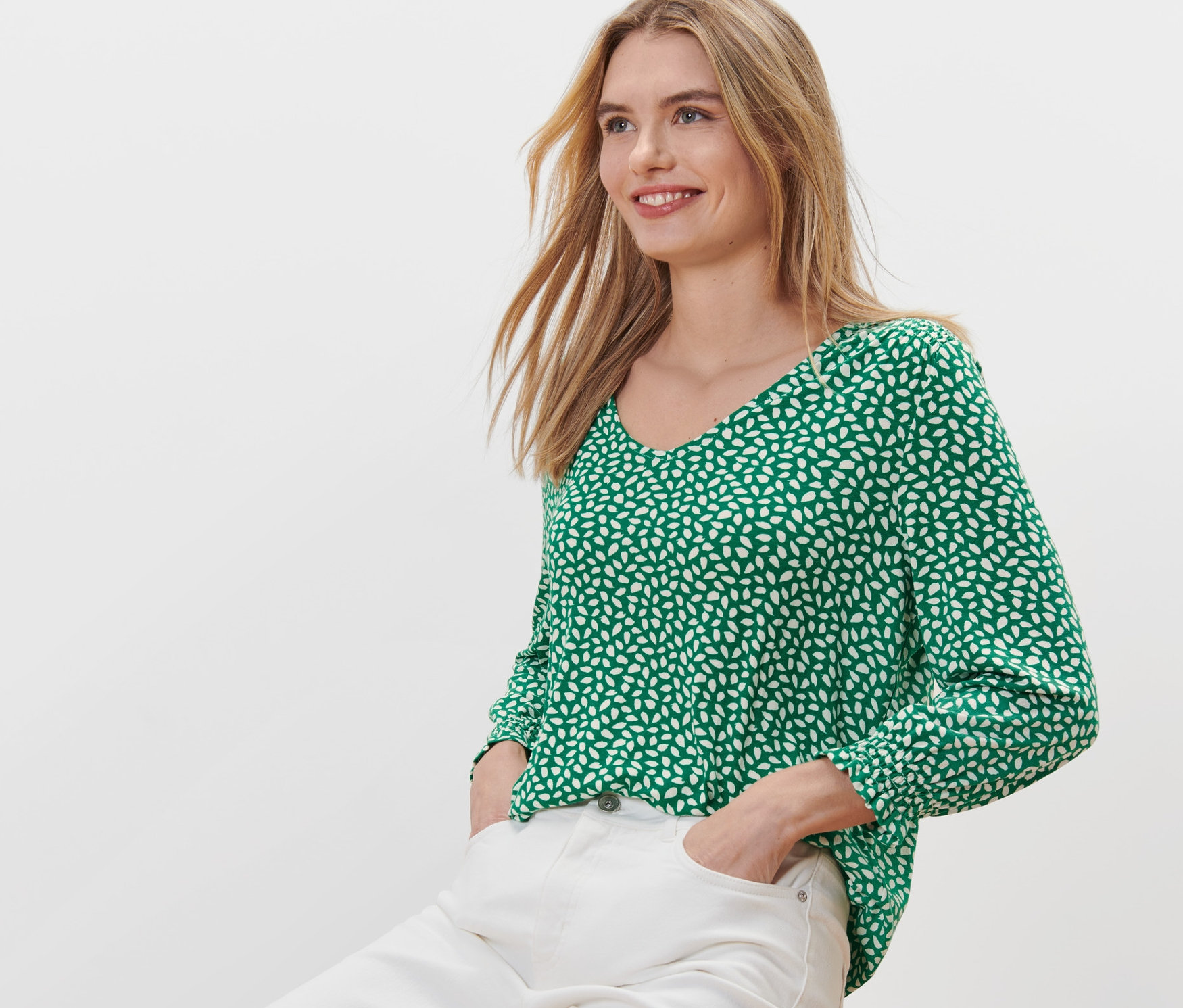 Žena sedí na stoličce a má na sobě zelené halenkové triko s potiskem.