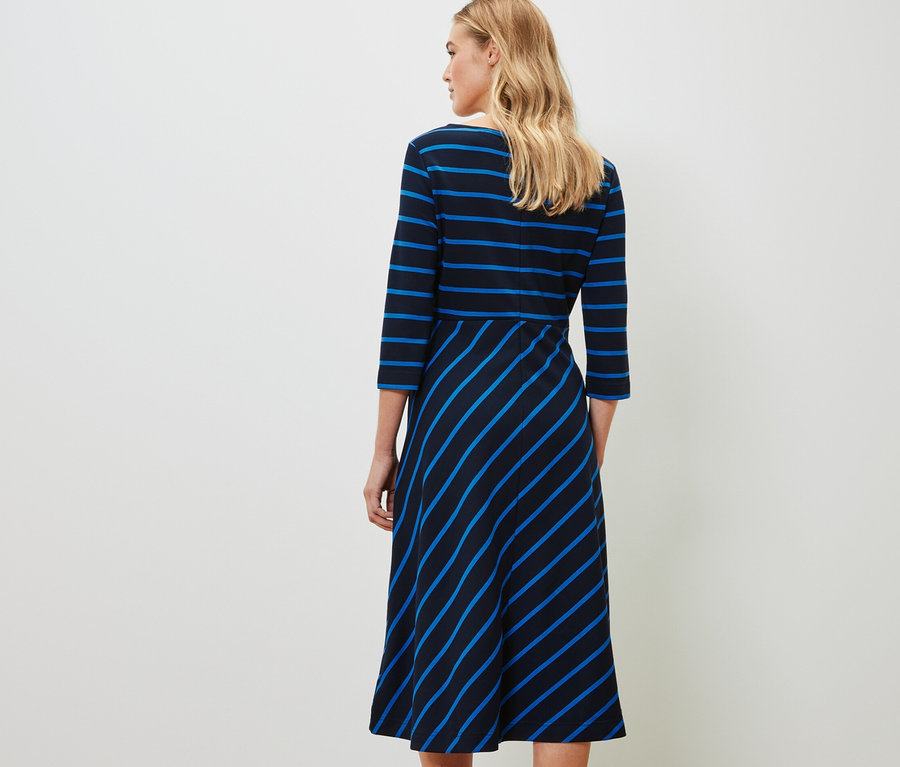 Žena stojí zády k fotoaparátu a má na sobě žerzejové šaty s proužky.