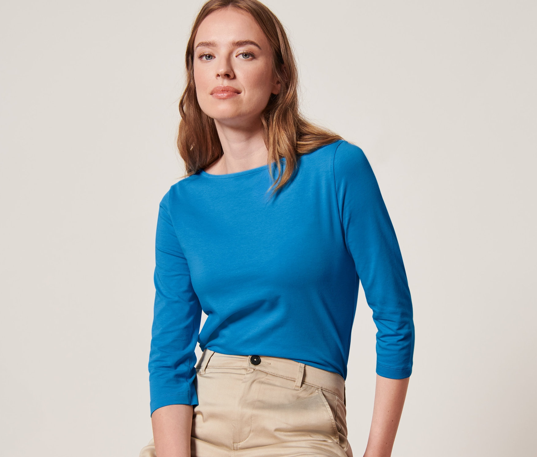 Žena sedí na stoličce a má na sobě azurově modré triko s 3/4 rukávem.