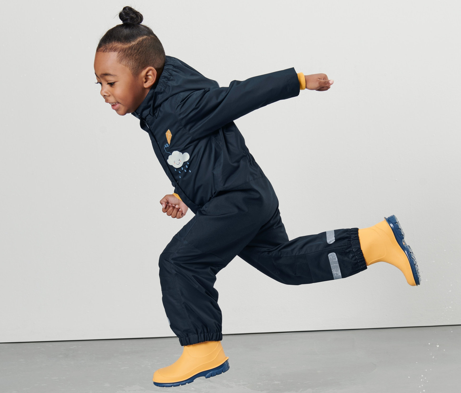 Chlapec v dětské kombinéze do deště skáče v kaluži.