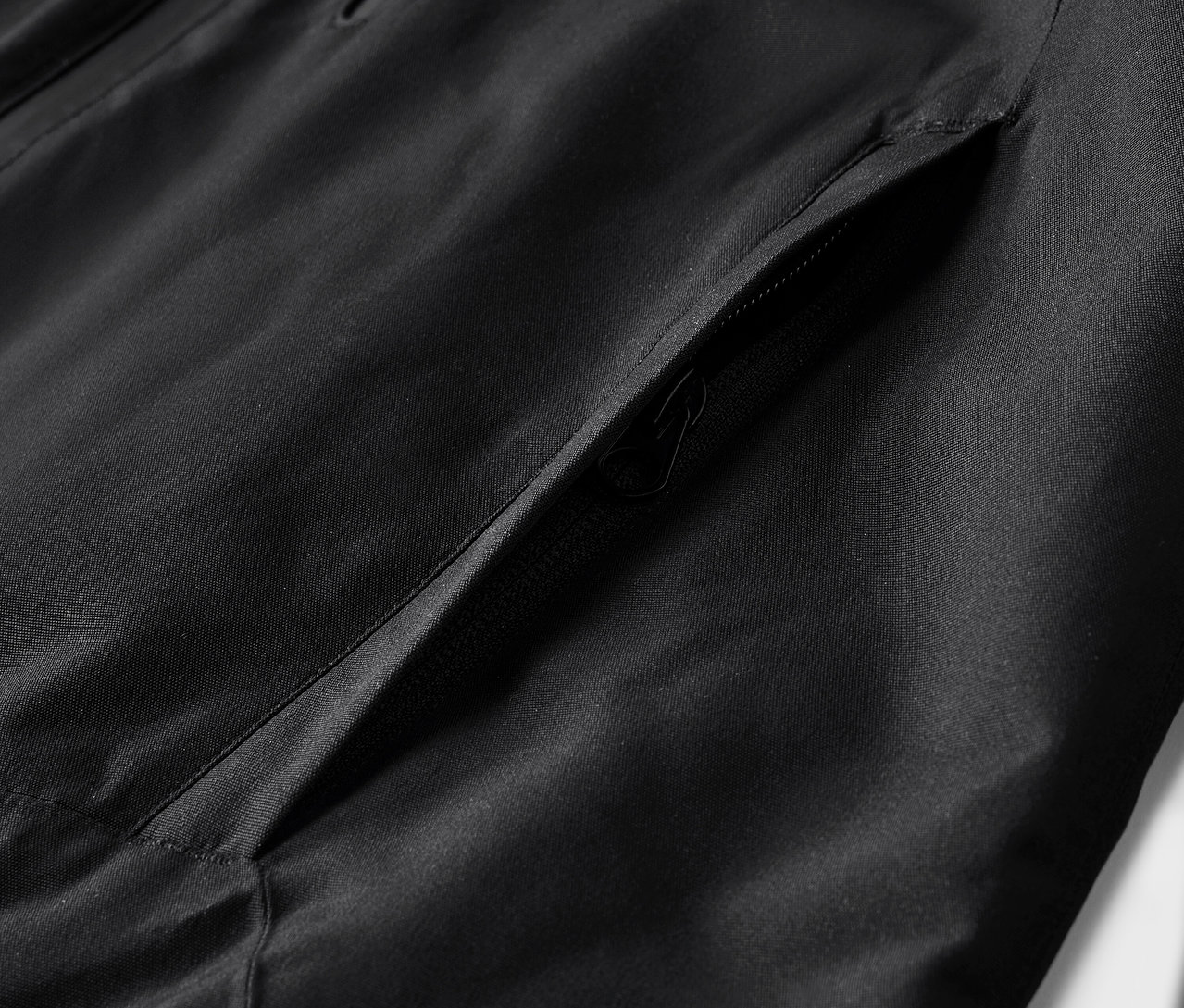 Detail černé bundy s kapsou.