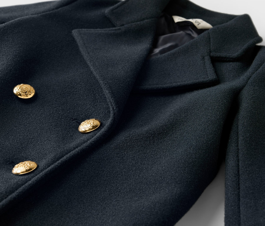 Detailní záběr na tmavě modrý dvouřadý kabát se zlatými knoflíky.