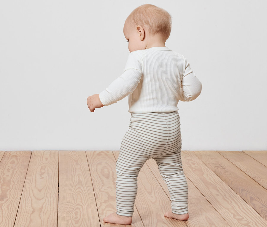 Batole chodí po dřevěné podlaze a má na sobě pruhované dětské legíny, 5 ks.