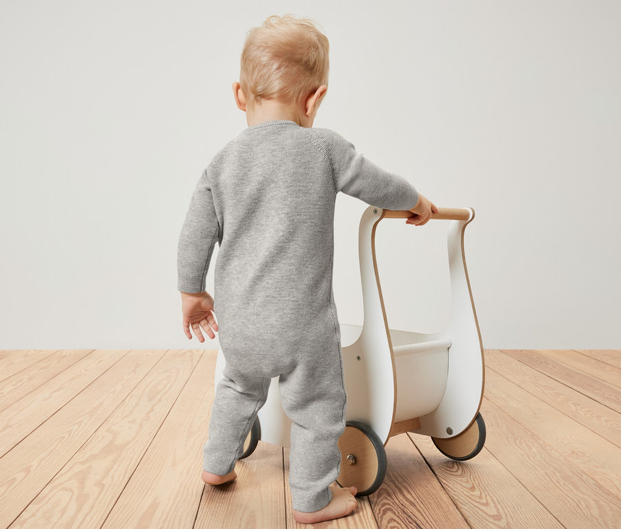 Dítě v pleteném overalu tlačí chodítko.
