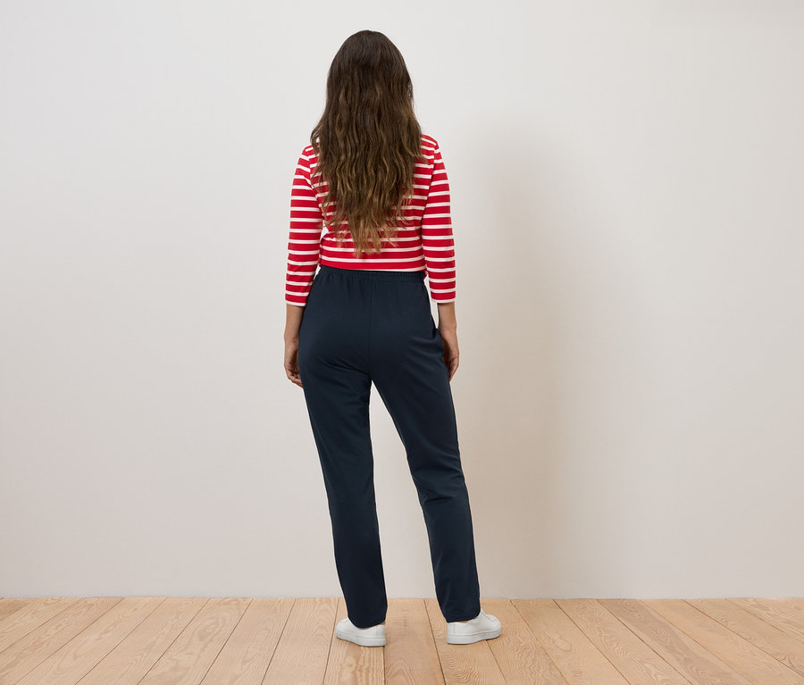 Žena v červeno-bílém pruhovaném topu a tmavě modrých kalhotách stojí zády k fotoaparátu.