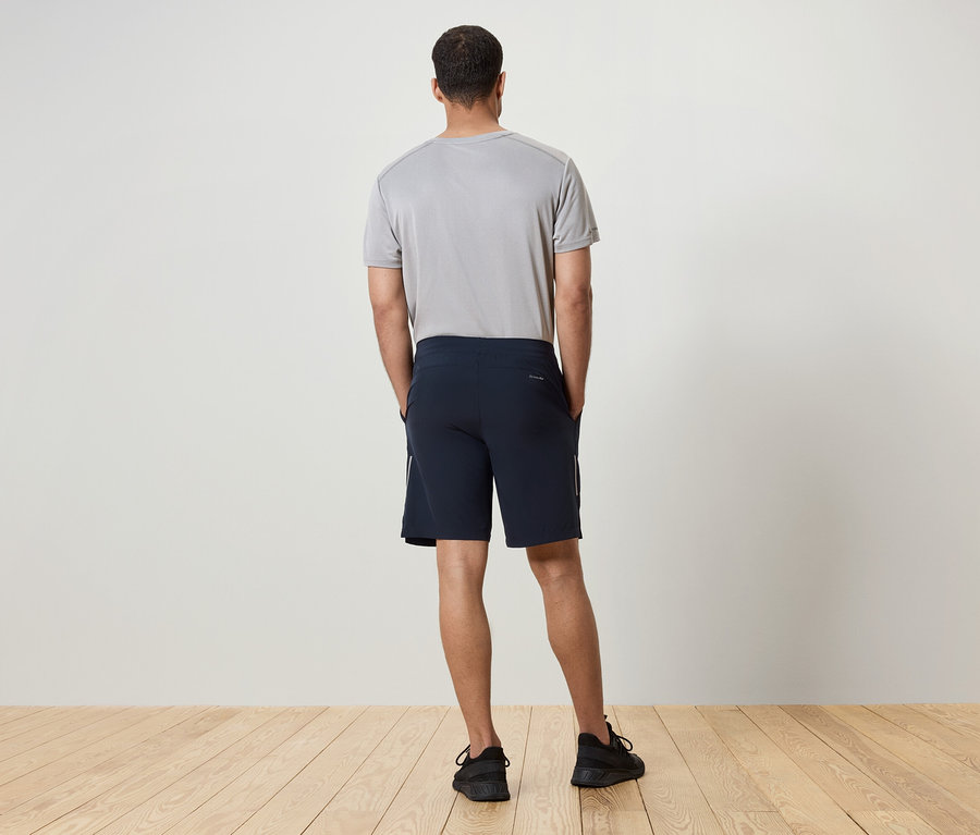Muž zády ke kameře má na sobě šedé tričko, tmavě modré šortky a černé tenisky.