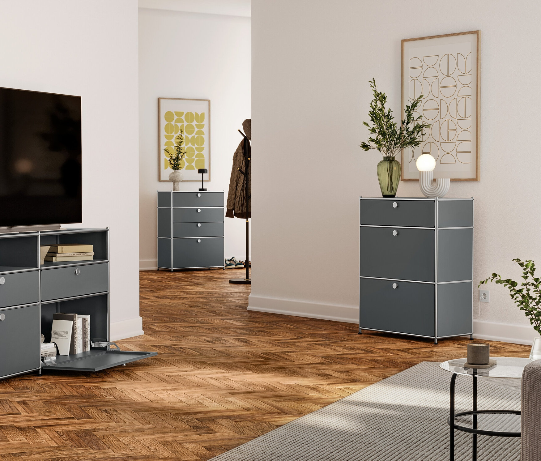 Obývací pokoj s televizí na šedé kovové komodě se zásuvkami a otevřenými policemi. V pozadí šedá komoda se třemi zásuvkami a další v chodbě.