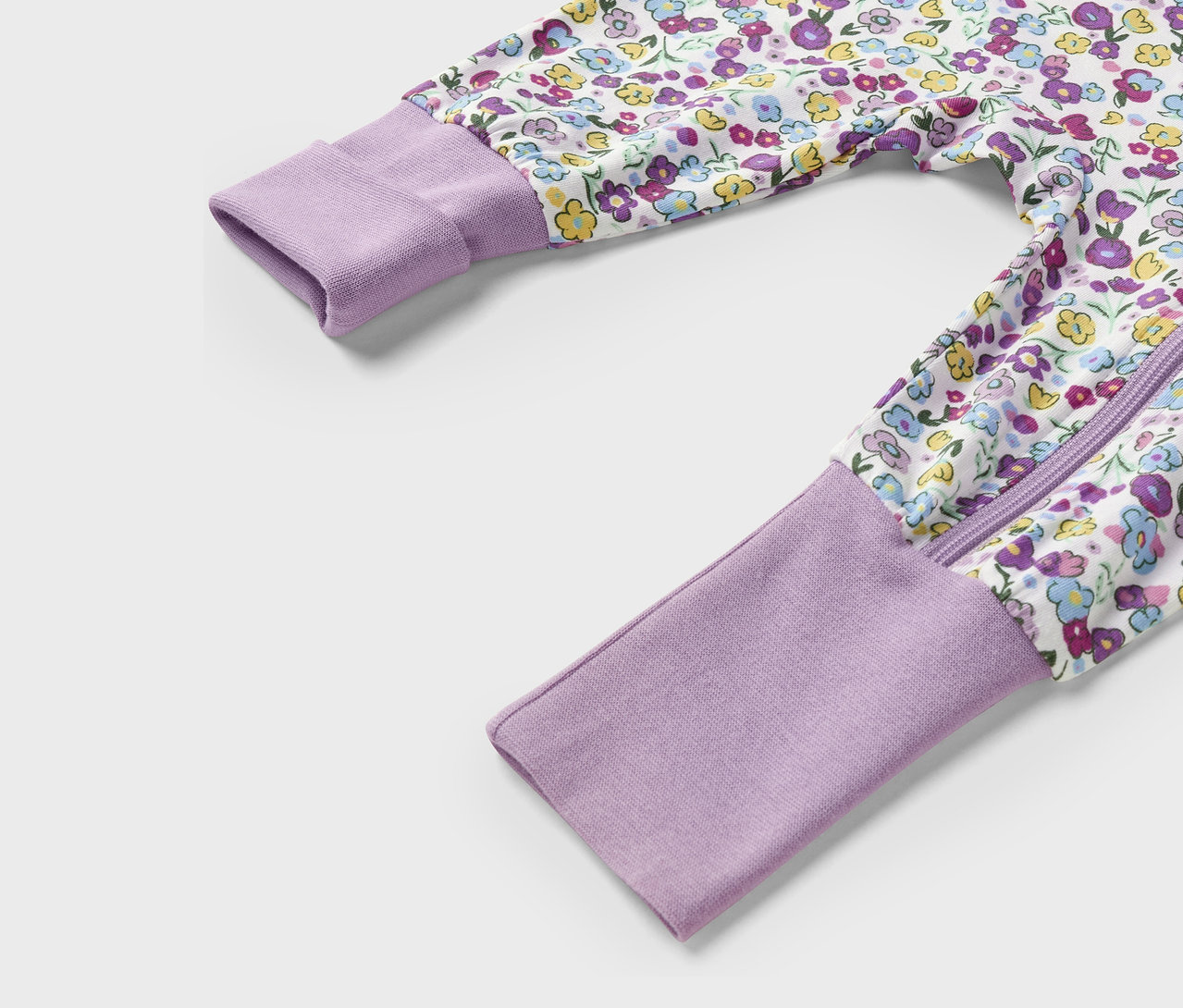 Detail fialového overalu s květinovým vzorem, zipem a dlouhými rukávy.