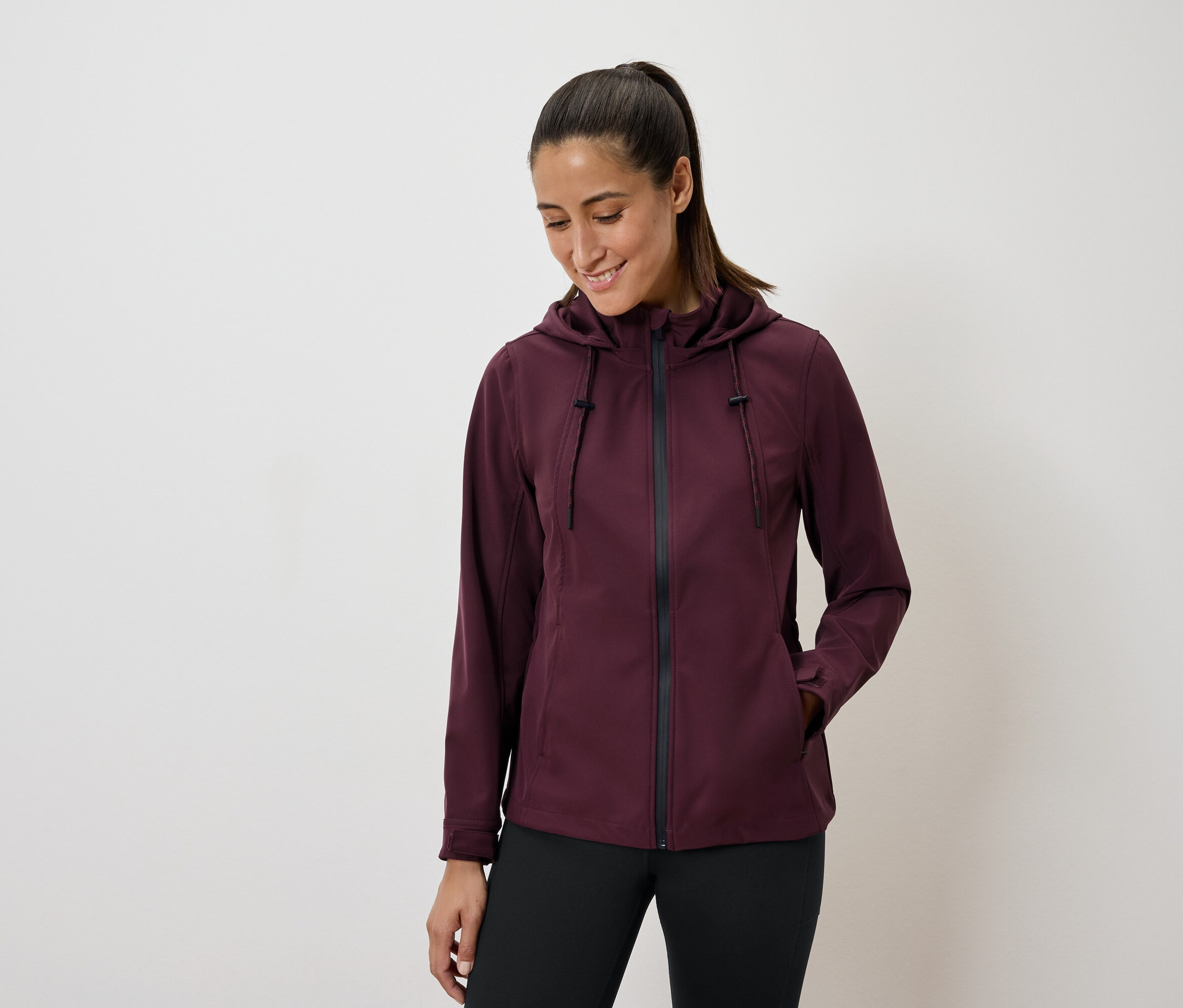 Žena v bordó bundě s kapucí a černých legínách.