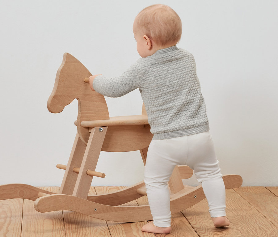 Batole v pleteném svetru se opírá o dřevěného houpacího koně.