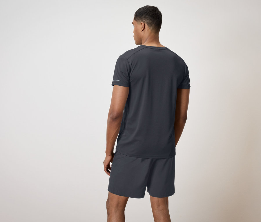 Muž v černém tričku a šortkách stojí zády k divákovi.