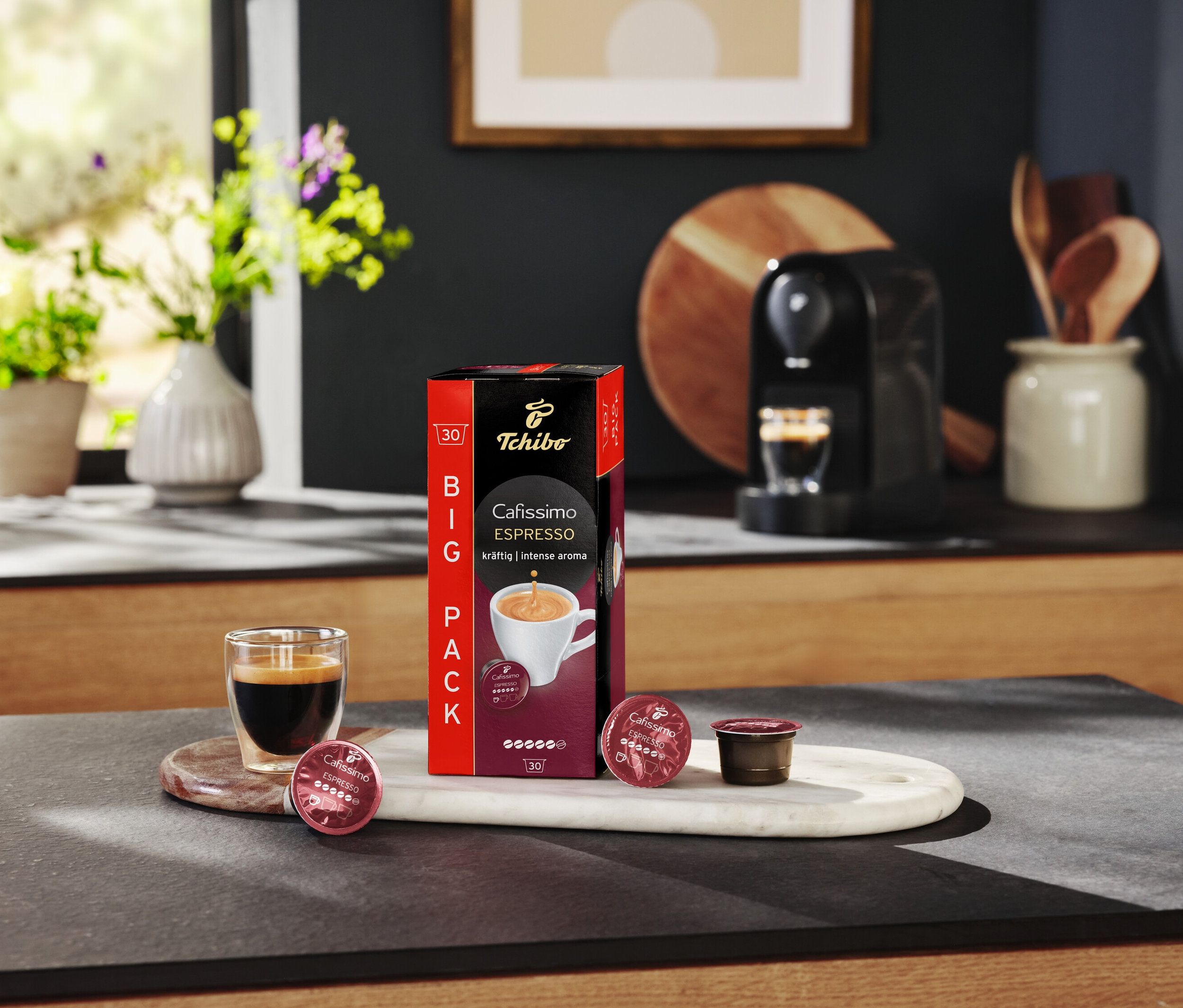 Espresso sklenice stojí vedle balení Cafissimo Espresso a kapslí na mramorovém tácku.