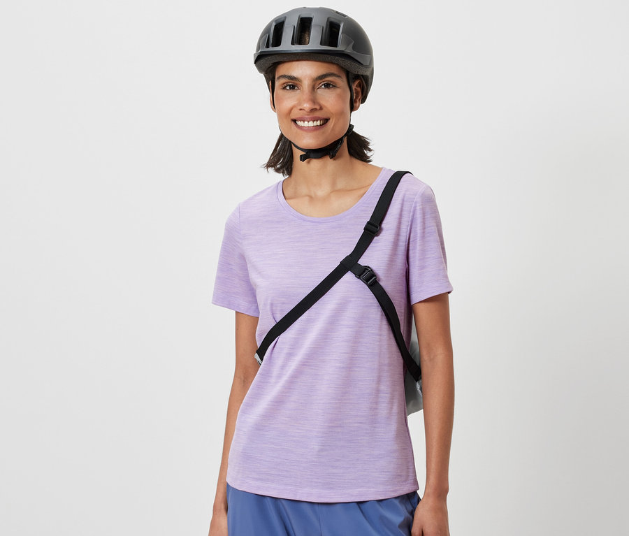 Usmívající se žena s cyklistickou helmou a nákupní taškou na kolo přes rameno.