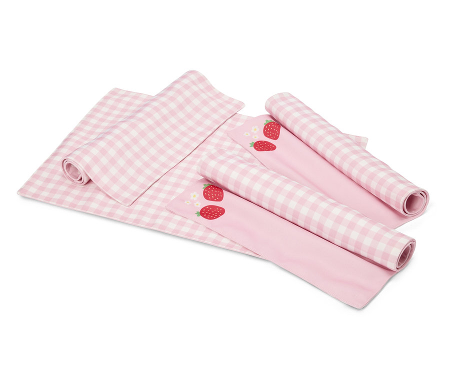 Na bílém pozadí leží růžovo-bílá kostkovaná deka a dvě růžové látky s motivy jahod, částečně srolované.