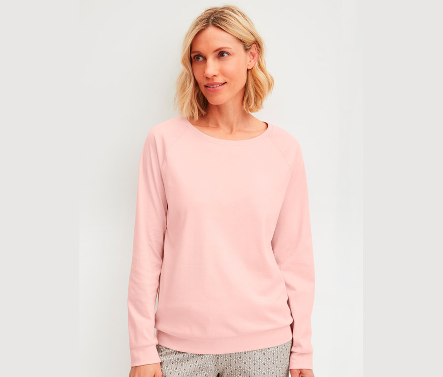 Žena s blond vlasy po ramena má na sobě růžovou blůzu s dlouhým rukávem.