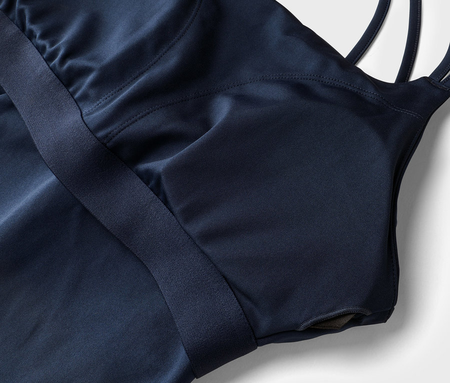 Detailní záběr na tmavě modrý sportovní top s ramínky a vestavěnou podprsenkou na bílém pozadí.
