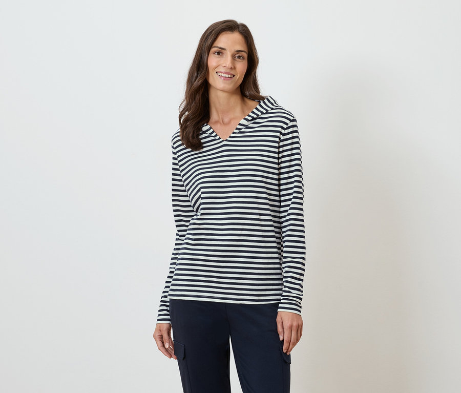 Žena má na sobě proužkovaný top s dlouhým rukávem a kapucí a tmavě modré kalhoty.