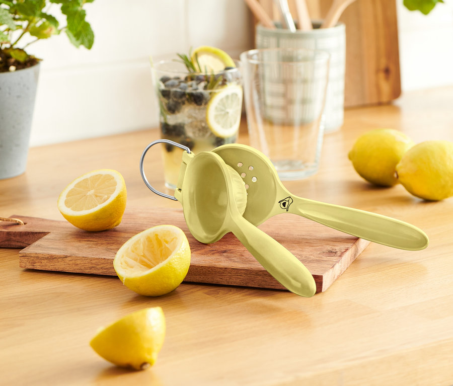 Na dřevěném stole je několik citronů, odšťavňovač citronů a sklenice limonády.