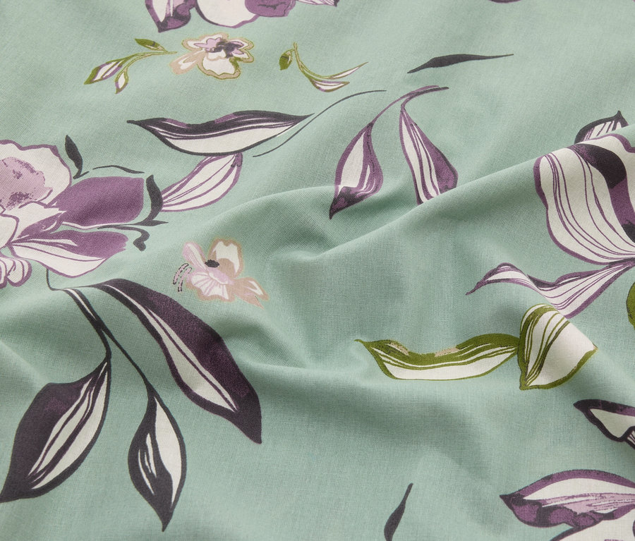 Detailní záběr mátové látky s květinovým vzorem v odstínech fialové, bílé a zelené.