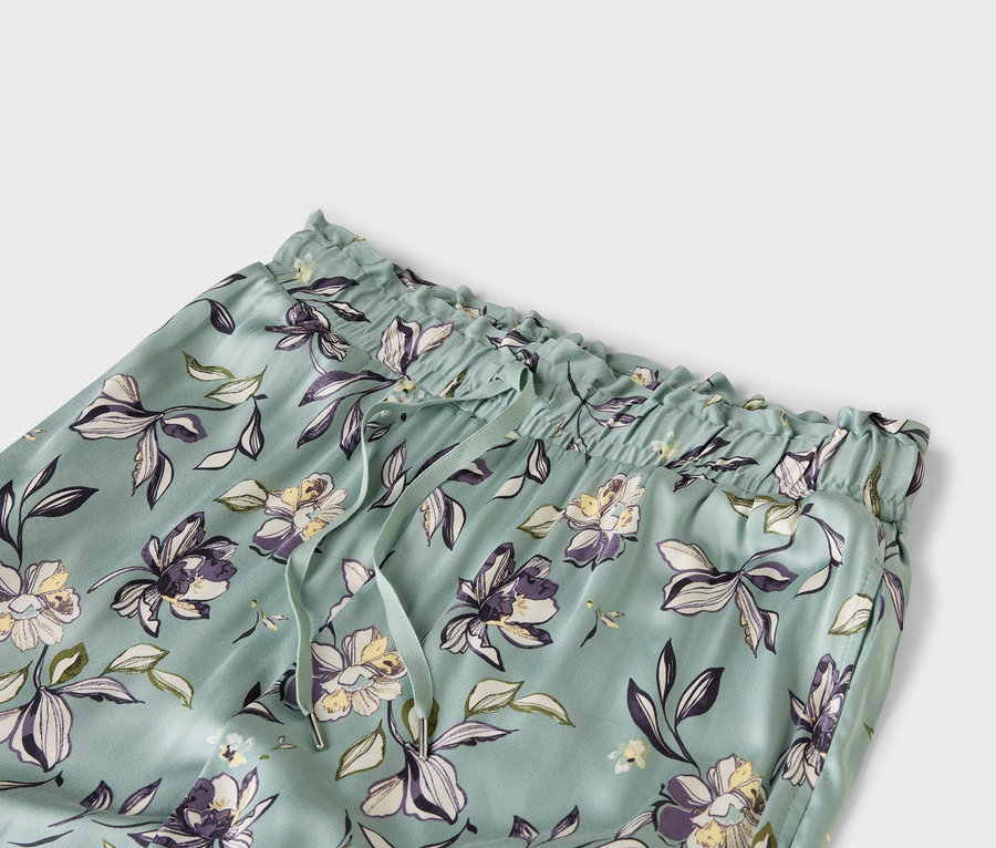 Detailní záběr na světle modré kalhoty s květinovým vzorem, elastickým pasem a stahovací šňůrkou.