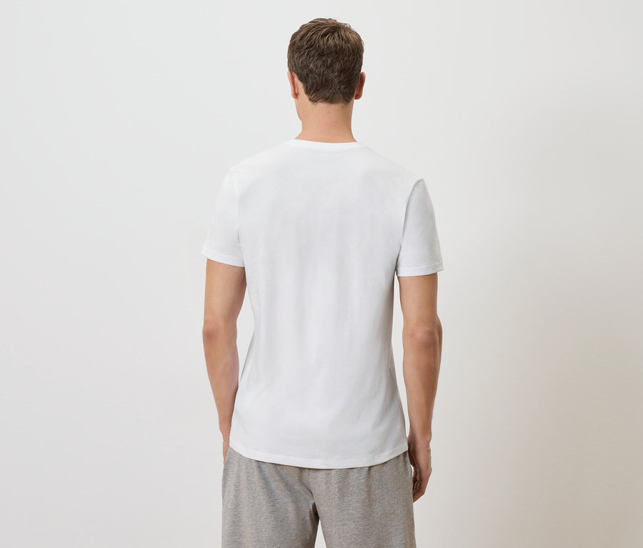 Muž stojí zády k fotoaparátu a má na sobě bílé tričko a šedé šortky.