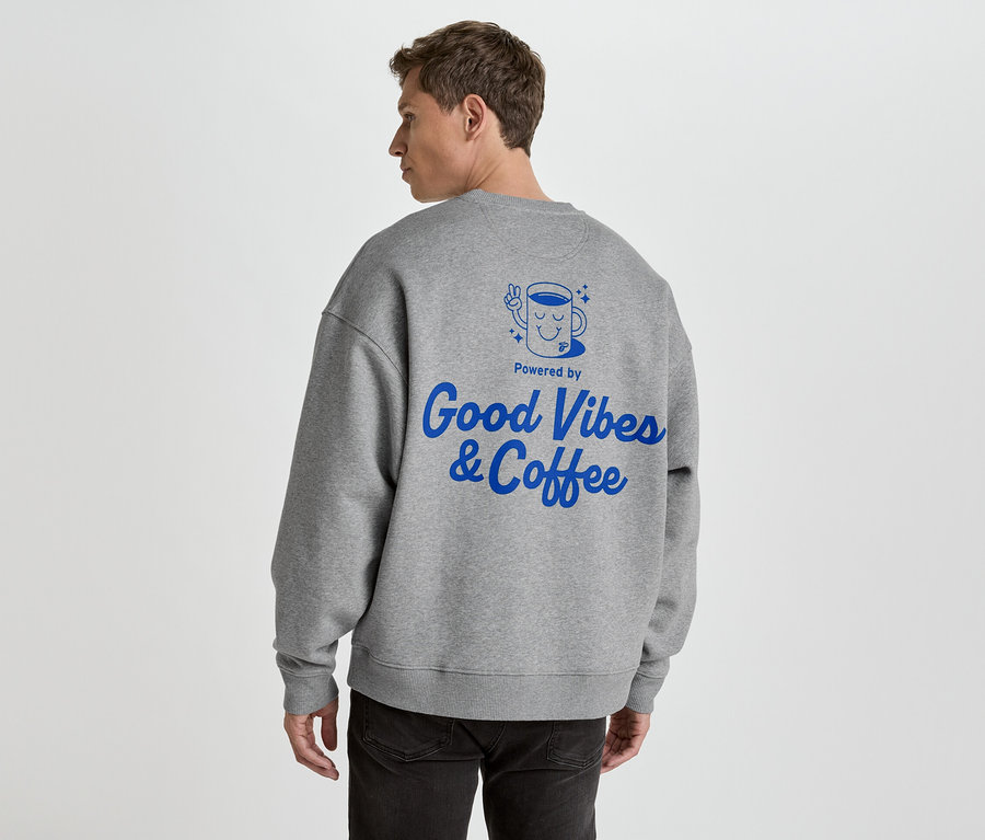 Muž zezadu v šedé mikině s modrým potiskem 'Good Vibes & Coffee'.