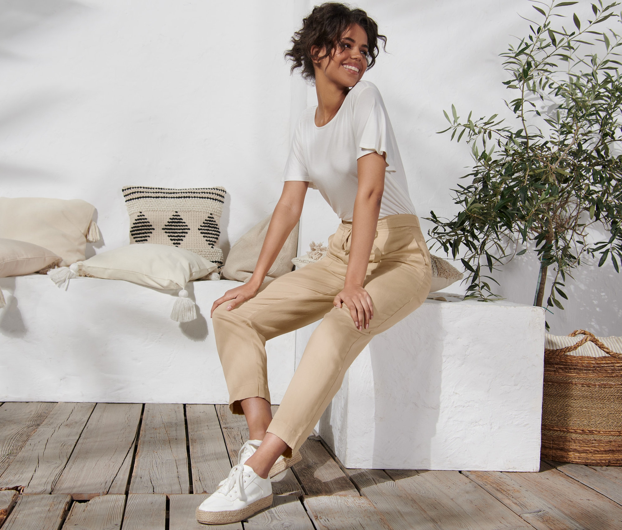 Žena sedí na bílém bloku a má na sobě lněné kalhoty.