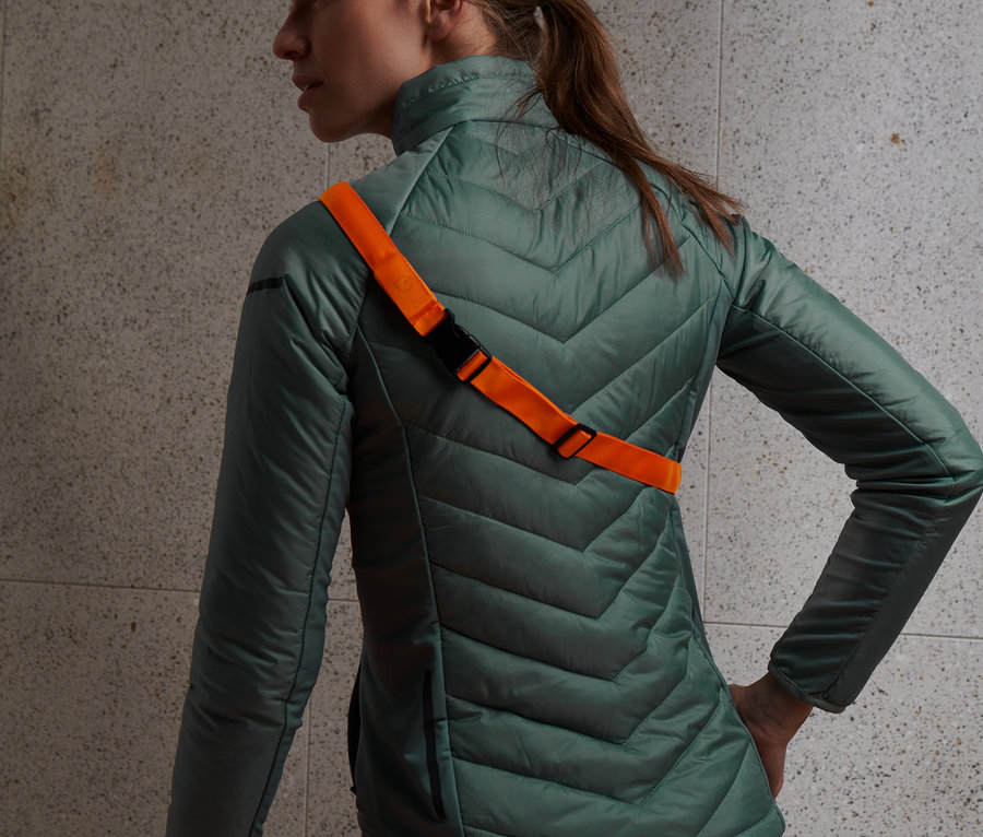 Žena má na sobě zelenou bundu a oranžový LED pásek.