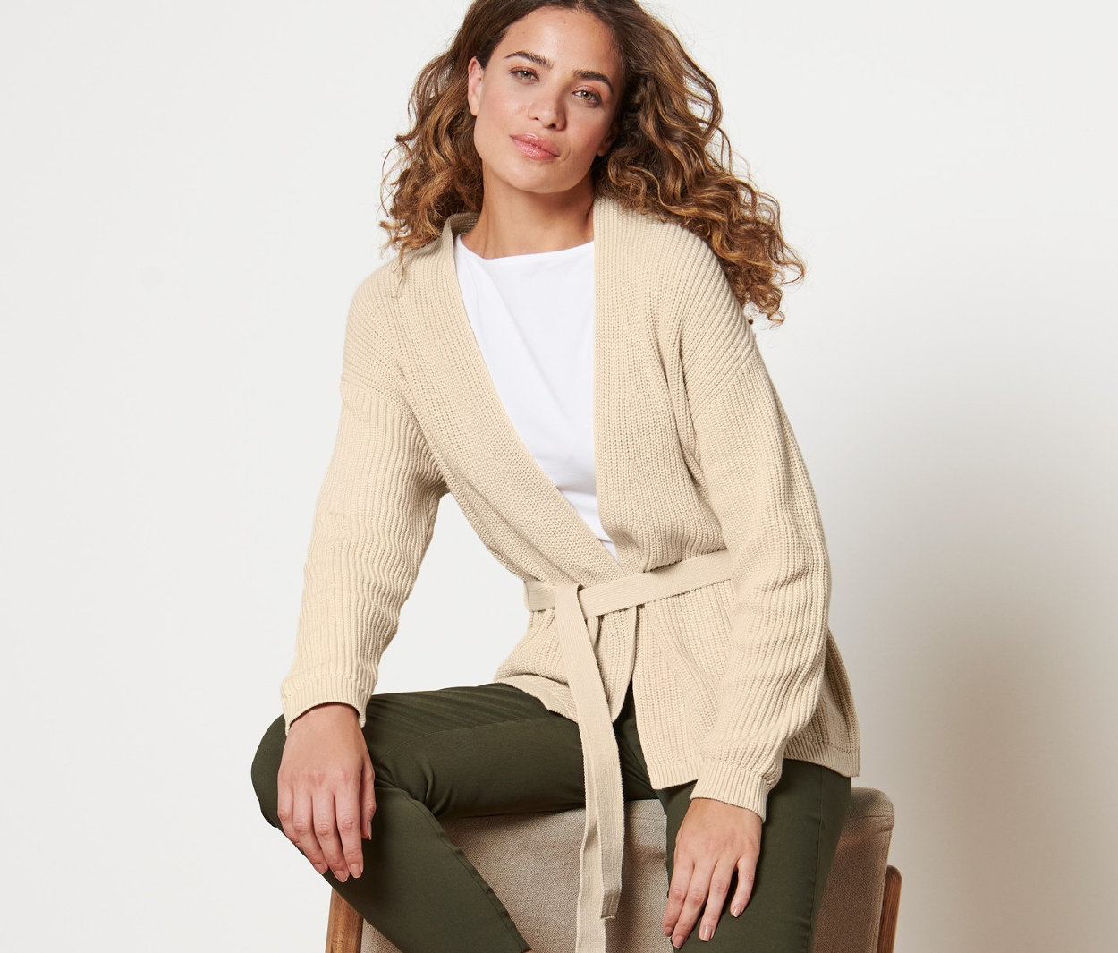 Žena sedí na židli a má na sobě zavinovací kardigan.