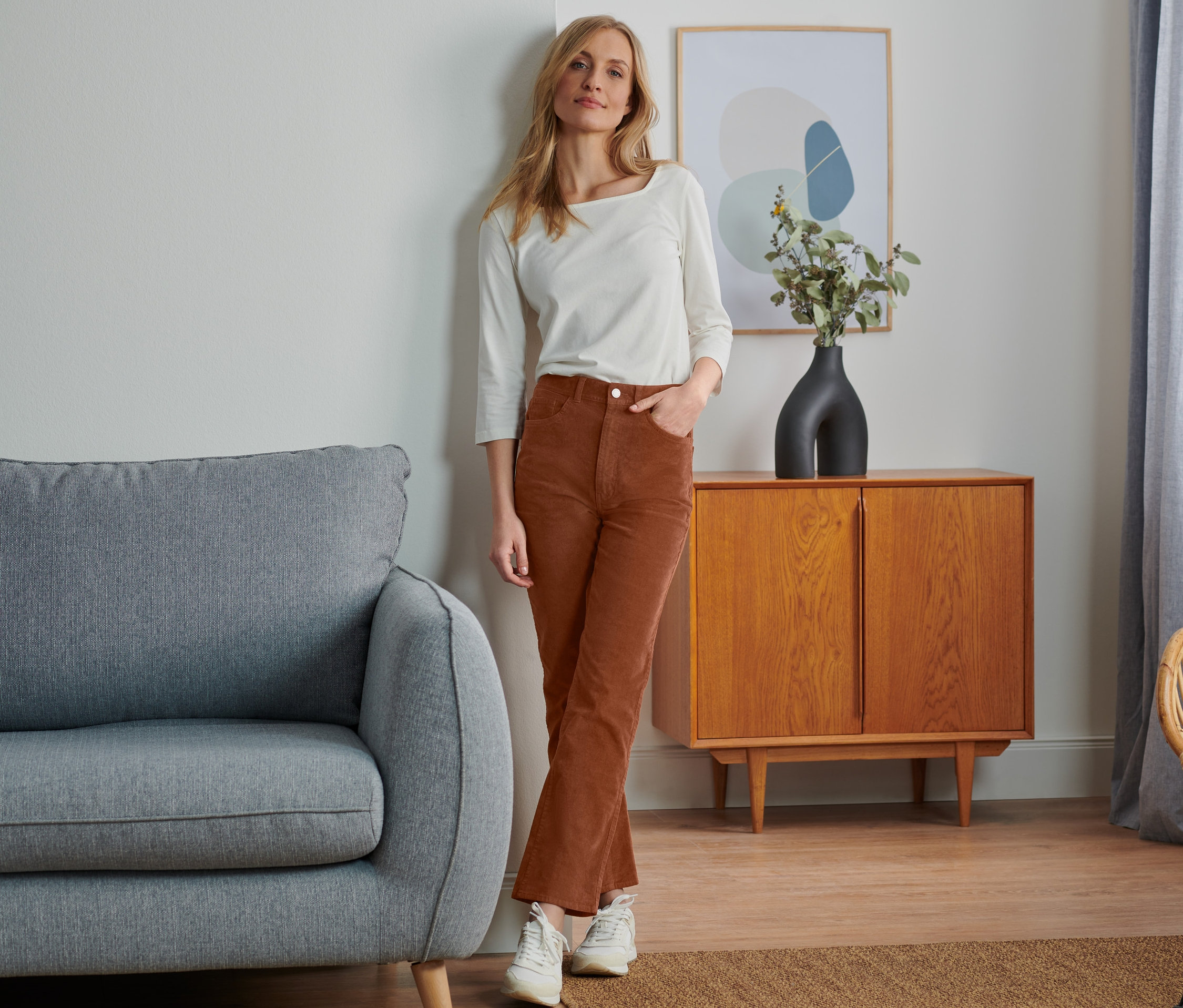 Žena pózuje v manšestrových kalhotách a bílém topu.