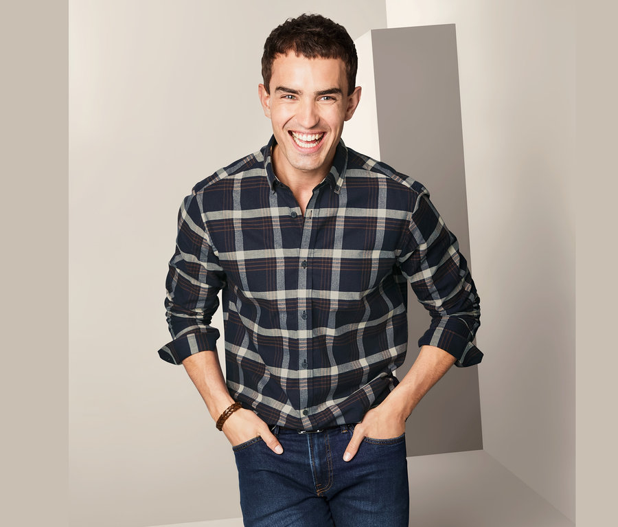 Muž se usmívá a pózuje v kostkované flanelové košili.