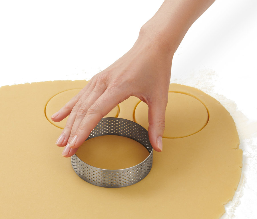 Ruka používá vykrajovátko na pečení z ušlechtilé oceli k vykrajování koleček z těsta.