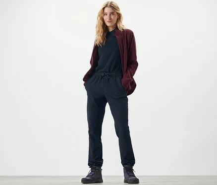 Blonďatá žena stojí a má ruce v kapsách softshellových kalhot joggpant.