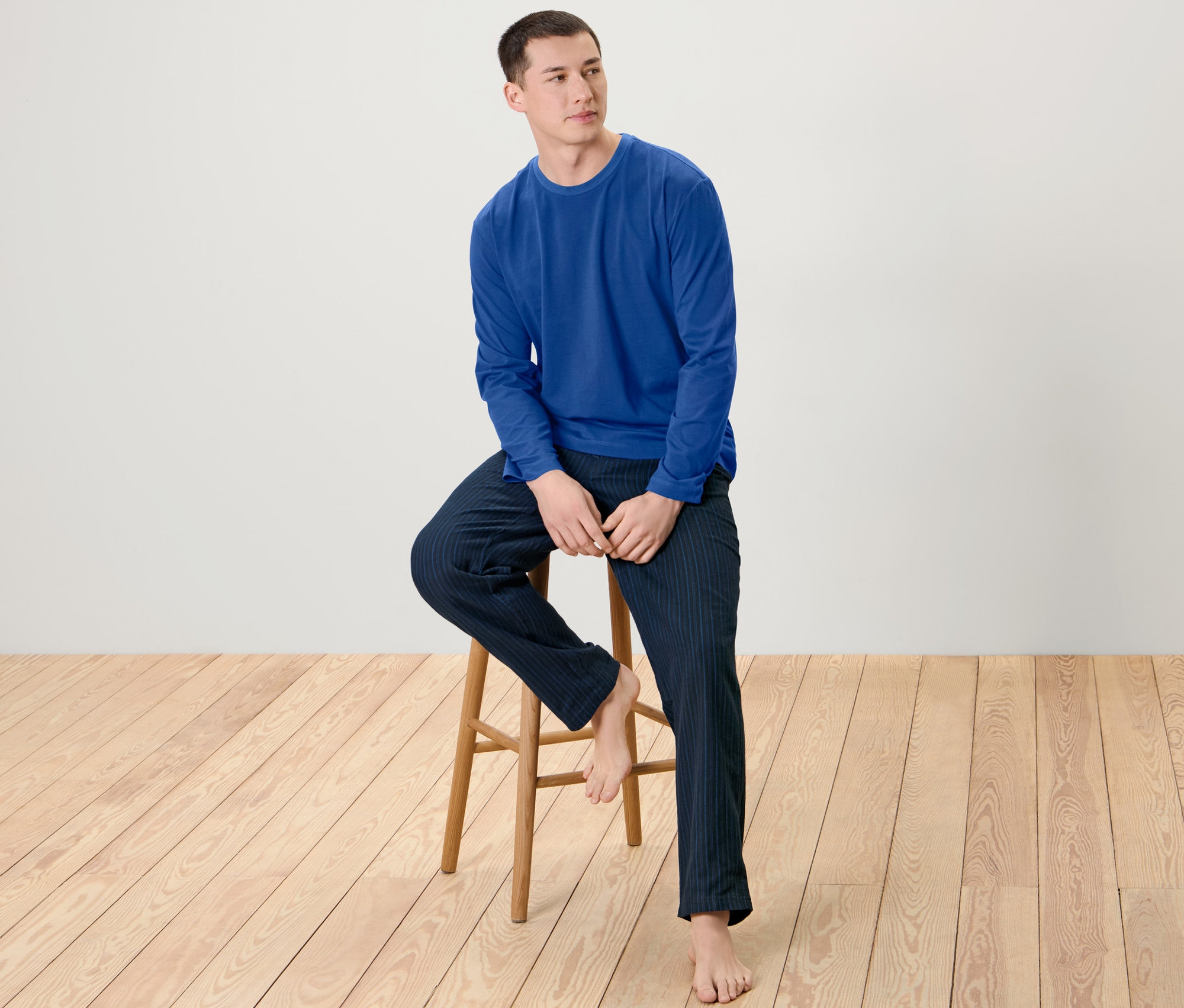 Muž sedí na dřevěné stoličce a má na sobě pánské pyžamo s flanelovými kalhotami.