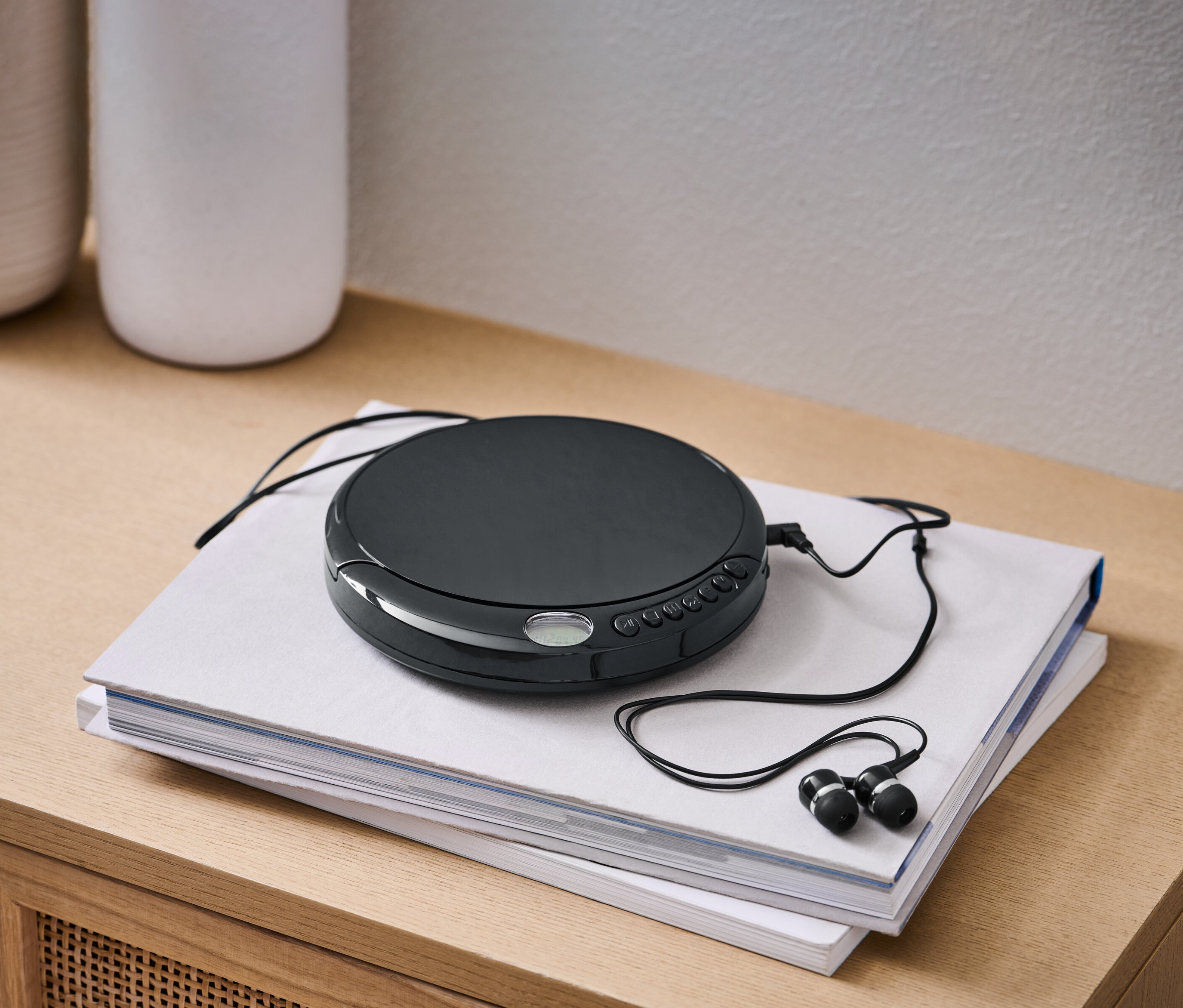 Černý přenosný CD přehrávač s černými sluchátky leží na dvou knihách.